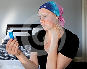 Portrait of a young cancer patient in a headscarf looks at bottle of pills with concern