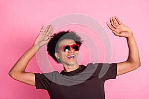 Portrait of young carefree man relax raised arms up chill out party wear sunglasses and brown t shirt islated on pink