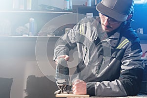 Portrait of a young carpenter joiner with electric jigsaw in the hands of a worker in a home workshop. Starting a