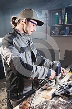 Portrait of a young carpenter joiner with electric milling cutter in the hands of a worker in a home workshop. Starting