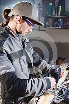 Portrait of a young carpenter joiner with electric milling cutter in the hands of a worker in a home workshop. Starting