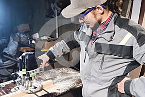 Portrait of a young carpenter joiner with electric milling cutter in the hands of a worker in a home workshop. Starting