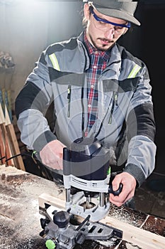 Portrait of a young carpenter joiner with electric milling cutter in the hands of a worker in a home workshop. Starting
