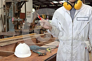 Portrait of young carpenter in white safety uniform holding a pencil in hands in wood workshop background. Industrial concept.