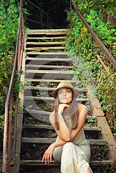 Portrait of a young casual woman in hat sitting on a vintage wooden stairs outdoor.