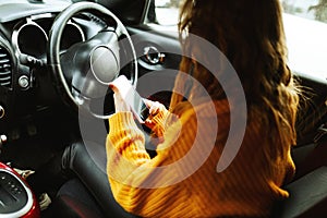 Portrait of a young casual woman in orange sweater texting on her smartphone or making video call while driving or