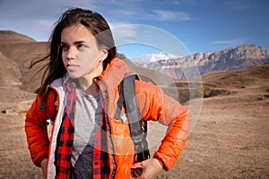 Portrait of a young Caucasian attractive woman standing in a backpack on the background of a rocky mountain peak looks