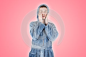 Portrait of young caucasian bearded man in blue bathrobe be scared isolated on pink background