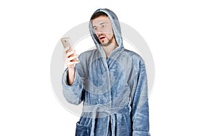 Portrait of young caucasian bearded man in blue bathrobe shows surprised emotion and watch to smartphone screen isolated on white