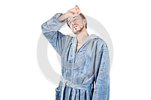 Portrait of young caucasian bearded man in blue bathrobe shows tired condition isolated on white background