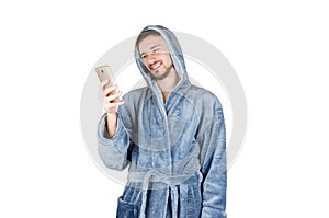 Portrait of young caucasian bearded man in blue bathrobe watching to smartphone screen isolated on white background