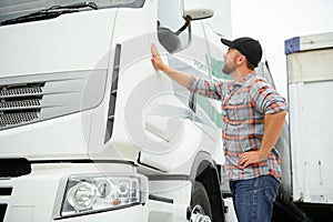 Portrait of young Caucasian bearded trucker standing by his truck vehicle. Transportation service. Truck driver job.