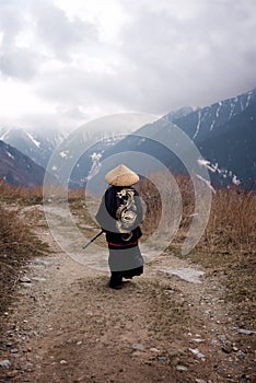 Rear view of a Young boy dressed as Samurai with the painted dragon on Kimono walking by the mountain trail in the cloudy weather