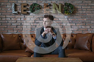 Portrait of young caucasian business man in formal suit sitting on brown sofa