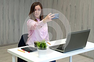 Young caucasian business woman in pink shirt in office doing selfie on the phone