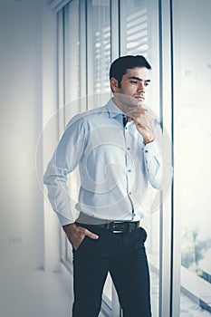 Portrait of young Caucasian businessman standing sad near a window in the office. Stressed and worried about the economic downturn