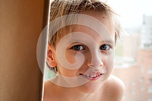 Portrait of a young Caucasian cute boy with blond hair inside the house near the window. A smiling, cheerful emotion