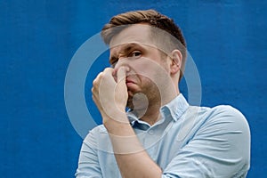 Portrait of young caucasian man closing his nose because of terrible smelling