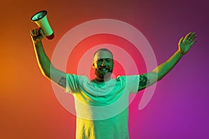 Portrait of young caucasian man with megaphone in raised hands isolated over gradient orange pink background in neon