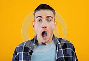 Portrait of young Caucasian man opening mouth in shock on orange studio background