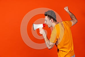 Portrait of young Caucasian man shouting at megaphone isolated on orange color studio background. Concept of human