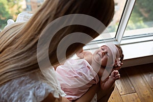 Portrait of young Caucasian mother holds hug little newborn baby two weeks old at home. Happy mom embraces small infant