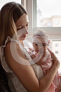 Portrait of young Caucasian mother holds hug little newborn baby two weeks old at home. Happy mom embraces small infant