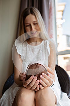 Portrait of young Caucasian mother holds hug little newborn baby two weeks old at home. Happy mom embraces small infant