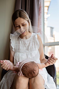 Portrait of young Caucasian mother holds hug little newborn baby two weeks old at home. Happy mom embraces small infant