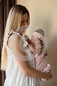 Portrait of young Caucasian mother holds hug little newborn baby two weeks old at home. Happy mom embraces small infant