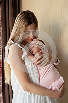 Portrait of young Caucasian mother holds hug little newborn baby two weeks old at home. Happy mom embraces small infant