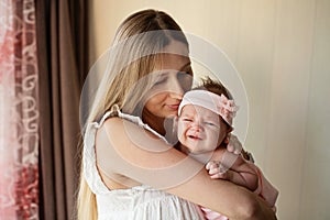 Portrait of young Caucasian mother holds hug little newborn baby two weeks old at home. Happy mom embraces small infant