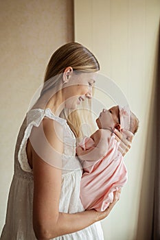 Portrait of young Caucasian mother holds hug little newborn baby two weeks old at home. Happy mom embraces small infant