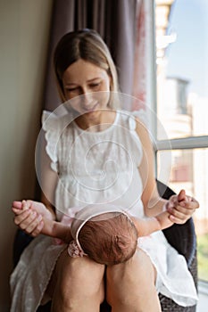 Portrait of young Caucasian mother holds hug little newborn baby two weeks old at home. Happy mom embraces small infant