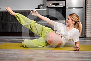 portrait of young caucasian pregnant woman lifting leg up, doing exercises on fitness mat