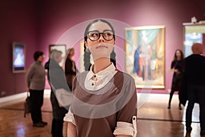 Portrait of young Caucasian pretty woman contemplates arts. Student visiting gallery or museum. Concept of education and