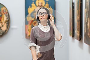 Portrait of young Caucasian pretty woman wearing headphones and contemplates ancient artefacts. Student visiting arts