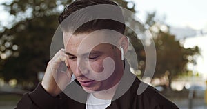 Portrait of young Caucasian student cheerful man with wireless headphone in ear having phone call and actively speaking