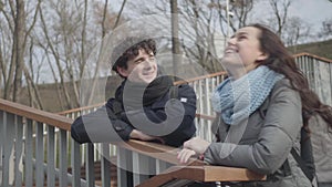 Portrait of young Caucasian students chatting and laughing in city park. Beautiful girl and handsome boy standing on