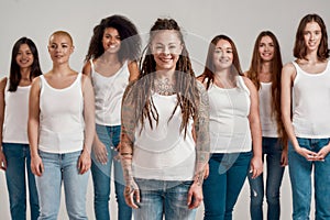 Portrait of young caucasian tattooed woman with dreadlocks in white shirt smiling at camera. Group of diverse women