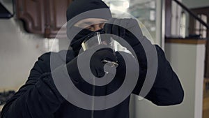Portrait of young caucasian thief in black clothes and balaclava drinking alcohol from the glass. The guy stealing