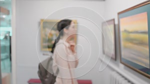 Portrait of young caucasian thoughtful woman looks at the painting. Exhibition in the art gallery. Slow motion