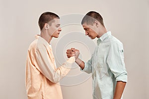 Portrait of young caucasian twin brothers looking at each other, holding hands while standing face to face isolated over