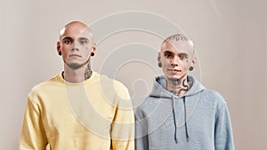 Portrait of young caucasian twin brothers with tattoos and piercings looking at camera while posing together in studio