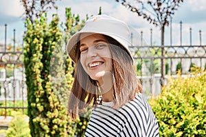 Portrait of young caucasian woman girl with toothy smile walking in green street outdoors looking at camera wearing in striped