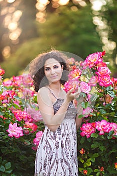 Portrait of a young Caucasian woman near red and pink roses bush in a rose garden, looking to the camera