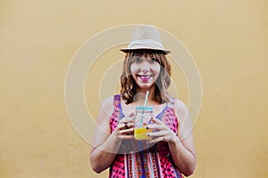 Portrait of young caucasian woman outdoors over yellow background enjoying a cup of healthy orange juice. summer time