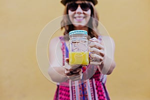 Portrait of young caucasian woman outdoors over yellow background enjoying a cup of healthy orange juice. summer time