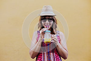 Portrait of young caucasian woman outdoors over yellow background enjoying a cup of healthy orange juice. summer time