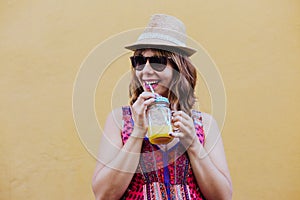 Portrait of young caucasian woman outdoors over yellow background enjoying a cup of healthy orange juice. summer time